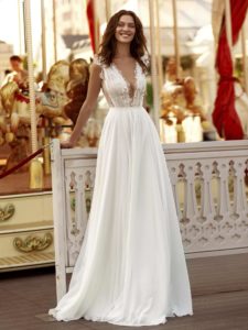 A bride in a deep V-neck chiffon gown with lace detailing, posing against vibrant architecture, embodying the charm of modern wedding dresses Toronto.