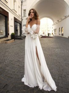 A bride in a romantic off-the-shoulder gown with floral-embroidered sheer sleeves and a thigh-high slit, showcasing the elegance of modern wedding dresses Toronto.