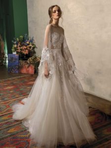 A-line wedding dress with deep V neckline, illusion panel on the chest, ruched fabric, and floral appliqué