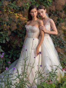 Strapless A-line wedding dress with frilled tulle neckline and a sequinned bodice and A-line wedding dress with bustier style corset, floral decor and pockets; available in ivory-nude, ivory