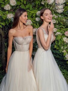 Strapless A-line wedding dress with frilled tulle neckline and a sequinned bodice and A-line wedding dress with bustier style corset, floral decor and pockets; available in ivory-nude, ivory