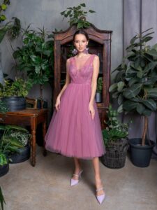 A woman is wearing a charming tulle cocktail dress in soft pink, featuring intricate embroidery on the bodice and a full, flowing skirt. This elegant piece is perfect for special occasions and is available by a Toronto Boutique of evening dresses.