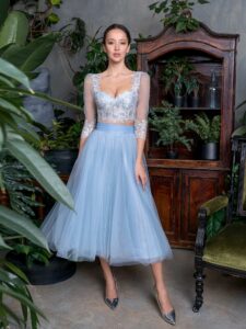 A woman is wearing a sophisticated two-piece set in pastel blue by Papilio Boutique, featuring a delicate lace crop top with sheer three-quarter sleeves and a floor-length, chiffon skirt. This ensemble is perfect for making a graceful statement at any formal event.