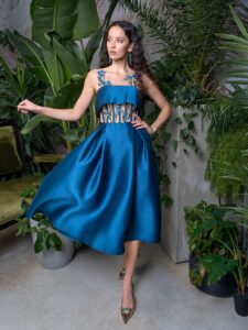A woman is wearing an A-line formal dress in a rich teal hue, featuring intricate floral embroidery and unique cut-out details, available from an evening dress store in Toronto. A stunning choice for sophisticated events.