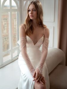 Atlas sheath wedding gown with long off-the-shoulder sleeves; available in ivory-peach