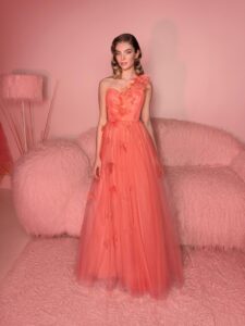 Style #821, one-shoulder A-line evening gown with 3D floral decor; available in coral (shown online), ivory, crimson, pink, blue, powder, black, red, green, cornflower blue, light green, sea green, watermelon, cherry, turquoise