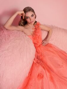 Style #821, one-shoulder A-line evening gown with 3D floral decor; available in coral (shown online), ivory, crimson, pink, blue, powder, black, red, green, cornflower blue, light green, sea green, watermelon, cherry, turquoise