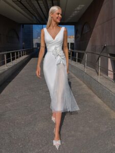 Cocktail-length wedding dress with a plunging V-neckline and a unique side floral appliqué, finished with a skirt tulle panel with pearls
