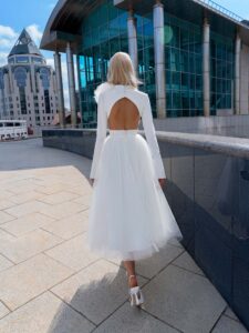Tea-length wedding dress with long sleeves and a keyhole open back, accented by a detachable tulle flower