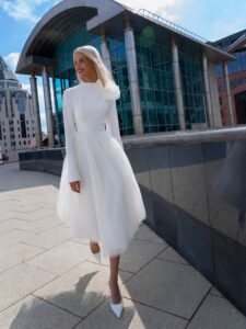 Tea-length wedding dress with long sleeves and a keyhole open back, accented by a detachable tulle flower
