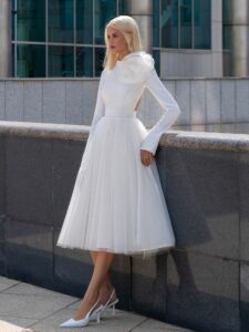 Tea-length wedding dress with long sleeves and a keyhole open back, accented by a detachable tulle flower