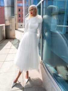 Tea-length wedding dress with long sleeves and a keyhole open back, accented by a detachable tulle flower