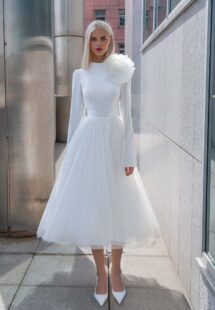 Style #16003, tea-length wedding dress with long sleeves and a keyhole open back, accented by a detachable tulle flower; available in ivory