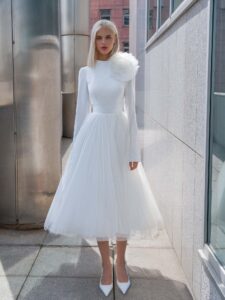 Tea-length wedding dress with long sleeves and a keyhole open back, accented by a detachable tulle flower