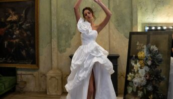 In a vintage-style room, a model showcases an avant-garde wedding dress with a voluminous ruffled high-low skirt and puffed sleeves, posing playfully under a grand chandelier, capturing one of the bold wedding dress styles by Papilio Boutique.