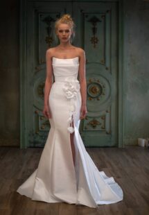Style #2500L, Mikado fit and flare wedding dress with a slit and detachable flower decor; available in ivory