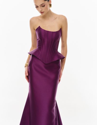 Angled view of plum mikado peplum corset dress offered at Papilio Boutique.